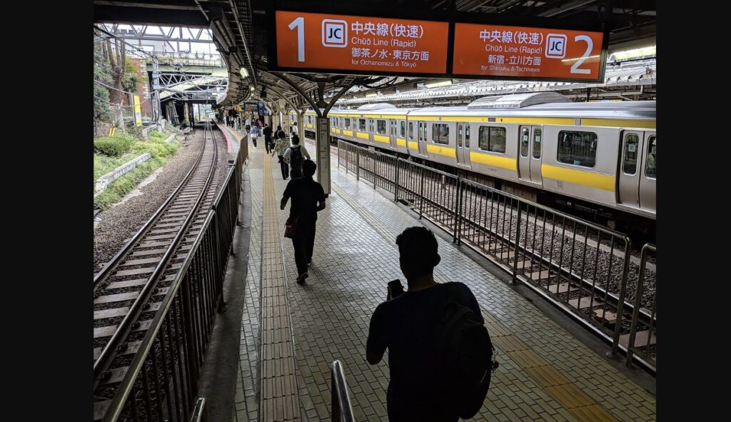 四ツ谷駅の中央線快速ホーム。オレンジ色の案内板があり、右側に中央・総武線の黄色い帯の電車が見える
